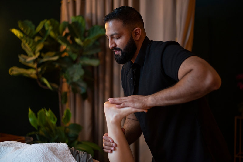 Arash holding a guest's raised leg at the ankle and calf, eyes on the work